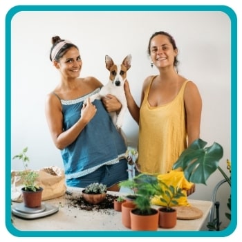 Two women holding and petting dog next to plants