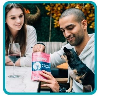 Couple sitting outside at table with wine and small dog with PupJoy treats