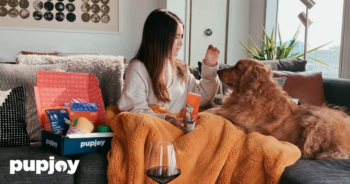 Woman sitting on couch with Golden Retriever opening a PupJoy box
